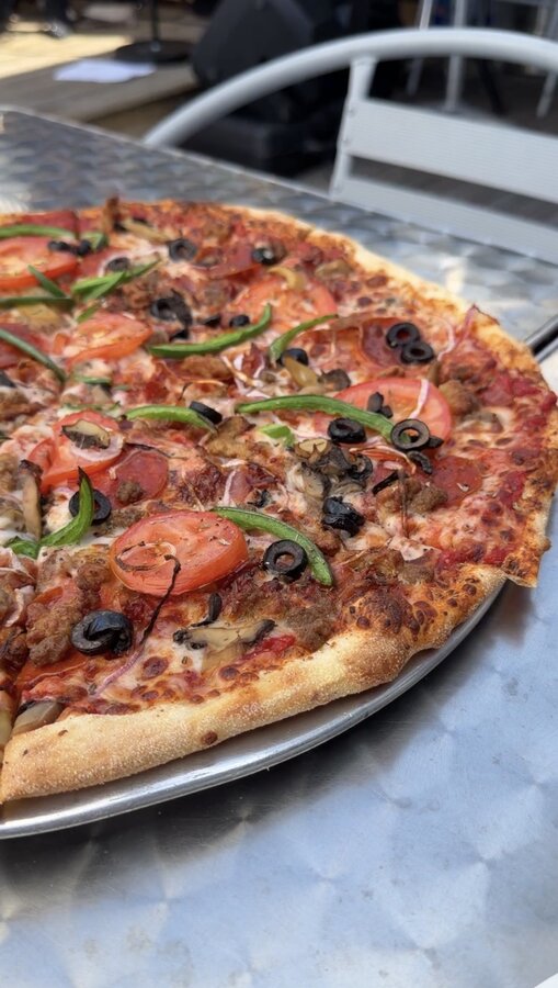 Loaded supreme pizza on a metal tray on the waterfront deck at Anchor Drafthouse & Pizzeria in Salter Path